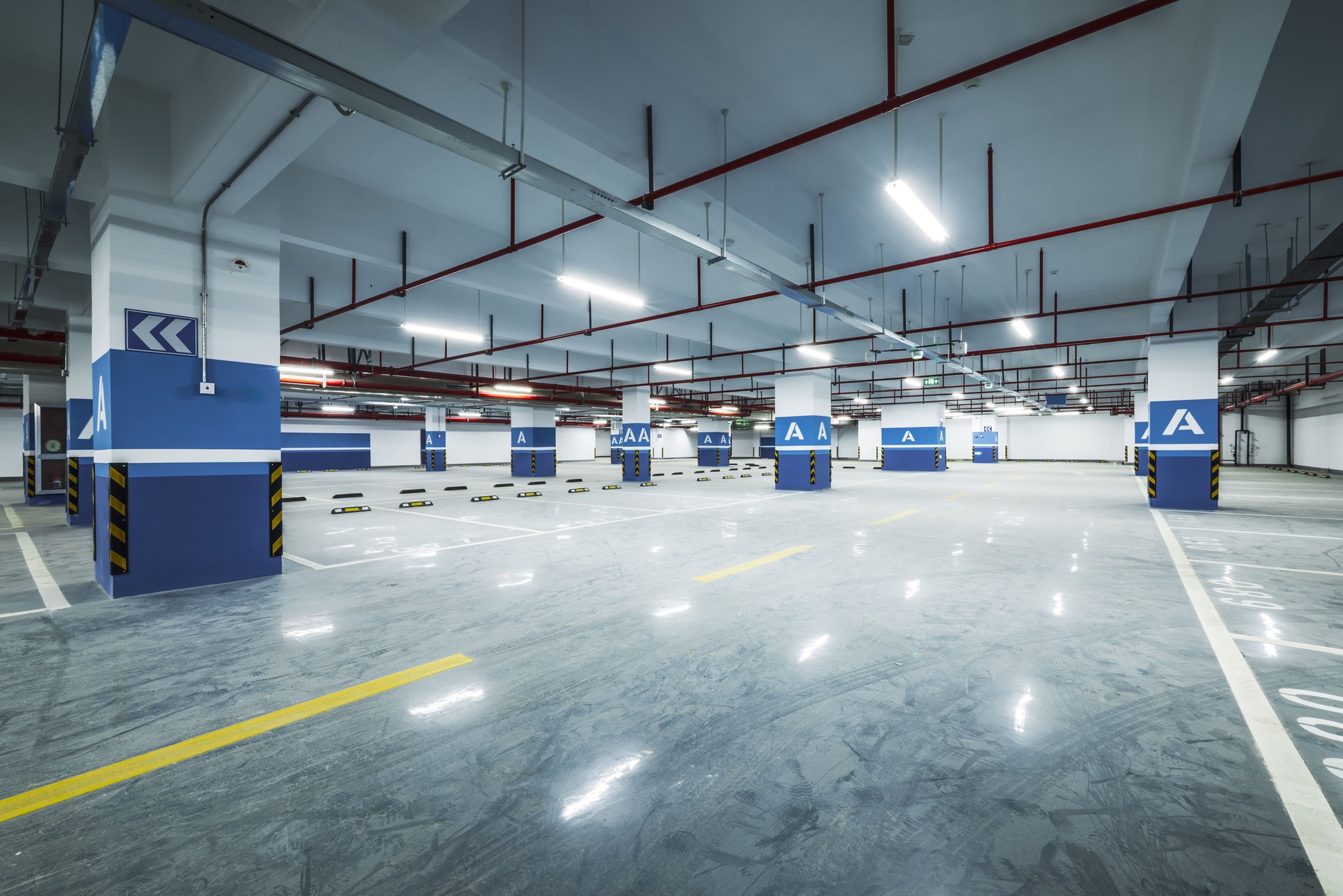 Brightly illuminated empty modern underground parking garage interior with concrete floor and pillars background.